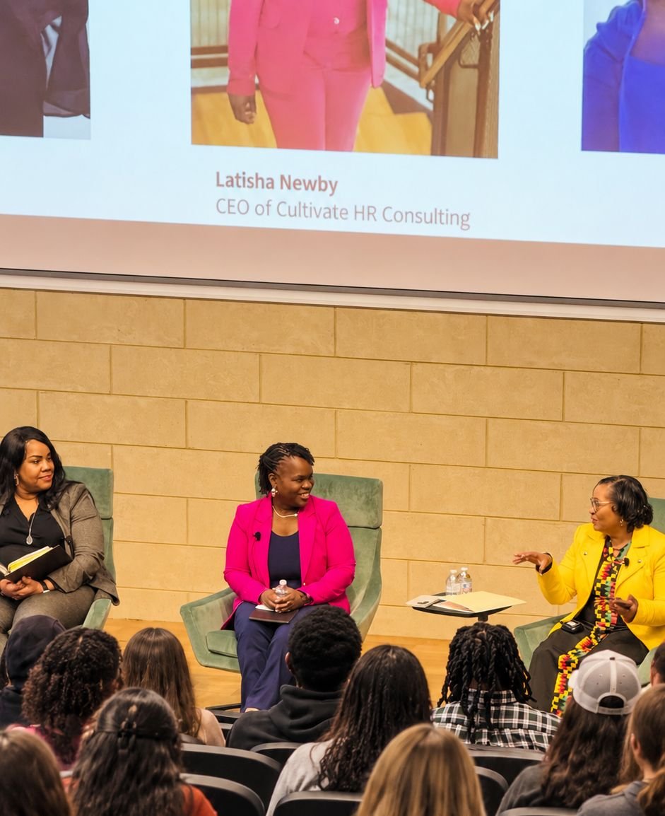 Latisha Newby on a panel in front of a student audience, with her name and title on the screen behind.