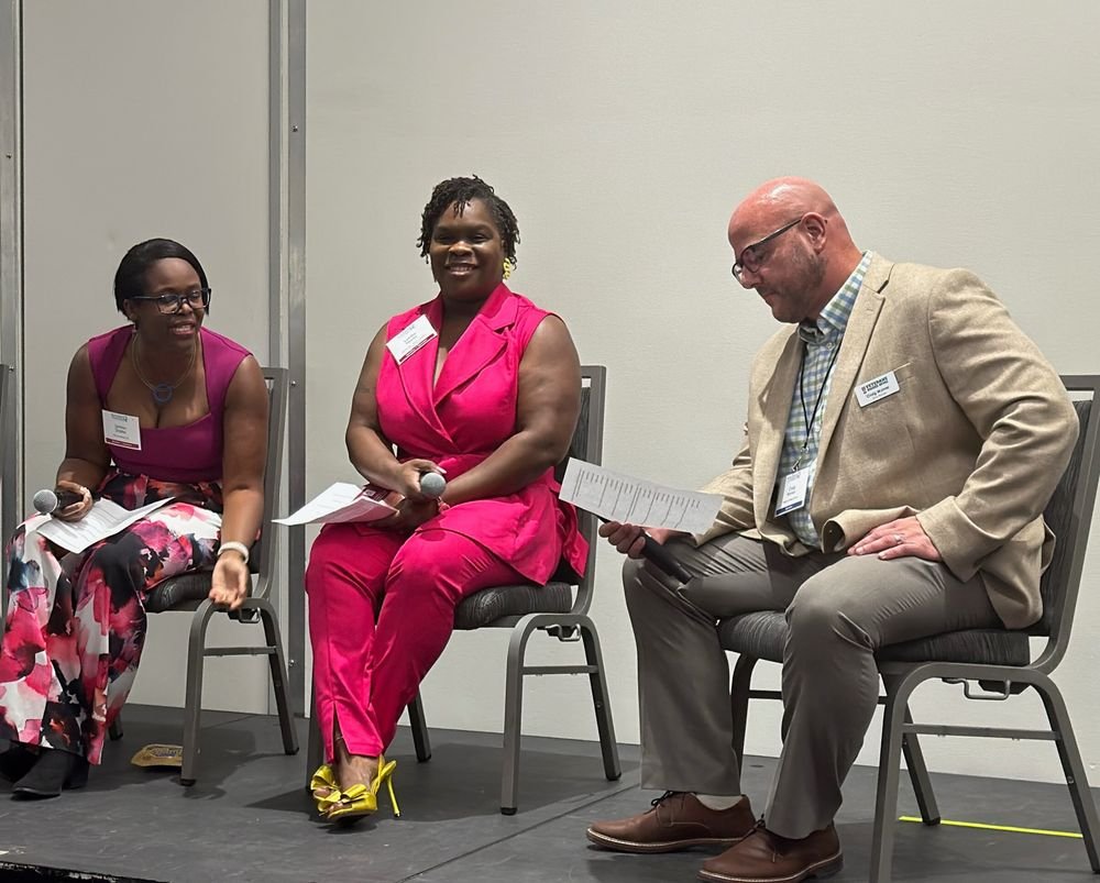 Latisha Newby holding the microphone on a three-person conference panel.